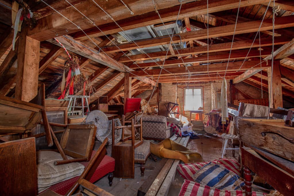 Grenier abandonné et encombré avec charpente en bois Grenier abandonné encombré de vieux meubles cassés, coussins rayés et débris sous une charpente en bois apparente. Lumière par une petite fenêtre.